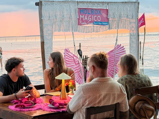 Amigos a la mesa bajo el letrero de Holbox Mágico con el cielo dorado