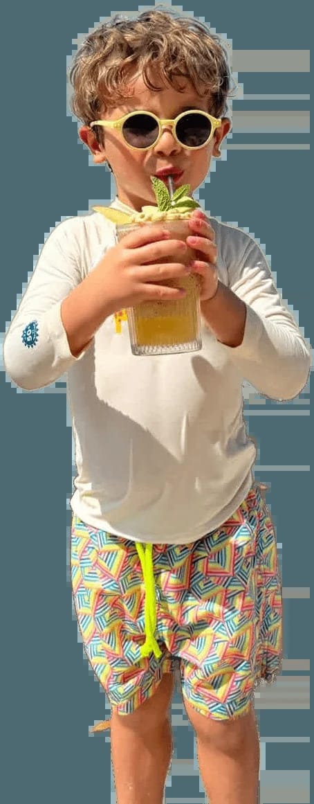 A boy in sunglasses sipping a drink by the sea